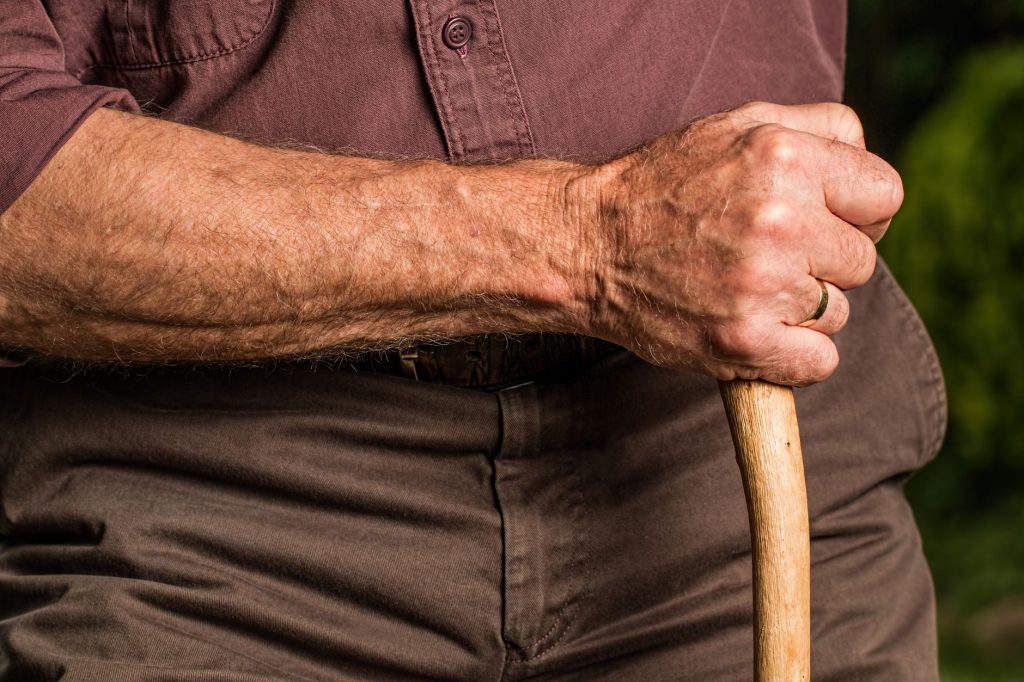 Main d’une personne âgée appuyée sur une canne, symbole de la perte d’autonomie